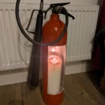 Angled front view of red fire extinguisher candle holder #3 showing the tall candle opening and original black fittings.
