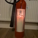 Close-up of the tall front opening in upcycled fire extinguisher candle holder #3 with a lit pillar candle inside.