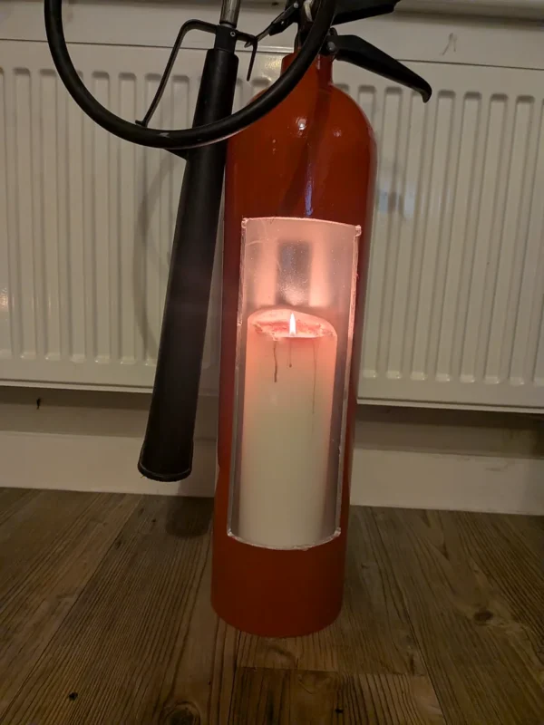 Close-up of the tall front opening in upcycled fire extinguisher candle holder #3 with a lit pillar candle inside.