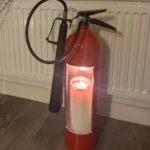 Fire extinguisher candle holder #3 in a home setting, showing its original looped hose, black horn and candlelit opening.