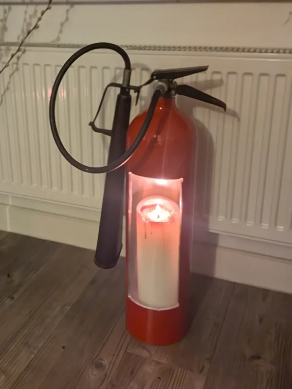 Fire extinguisher candle holder #3 in a home setting, showing its original looped hose, black horn and candlelit opening.