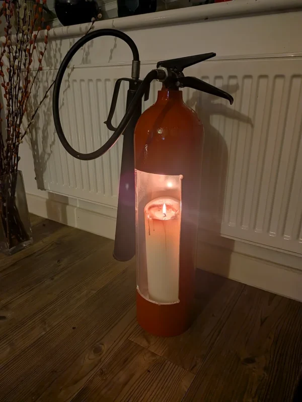Low-light view of red upcycled fire extinguisher candle holder #3 with a glowing pillar candle inside.