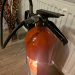 Angled detail of the handle, curved red shoulder and candle opening on upcycled fire extinguisher candle holder #3.