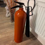 Rear view of upcycled red fire extinguisher candle holder #3 showing its original black hose and discharge horn.