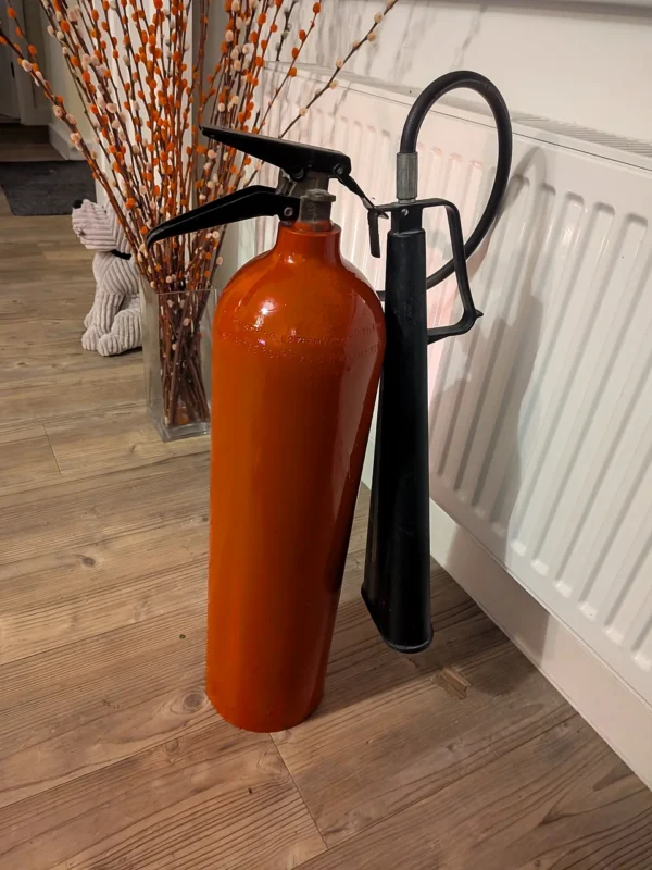 Rear view of upcycled red fire extinguisher candle holder #3 showing its original black hose and discharge horn.