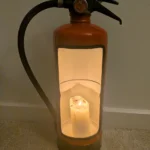 Red upcycled fire extinguisher candle holder with a glowing pillar candle and original black hose.