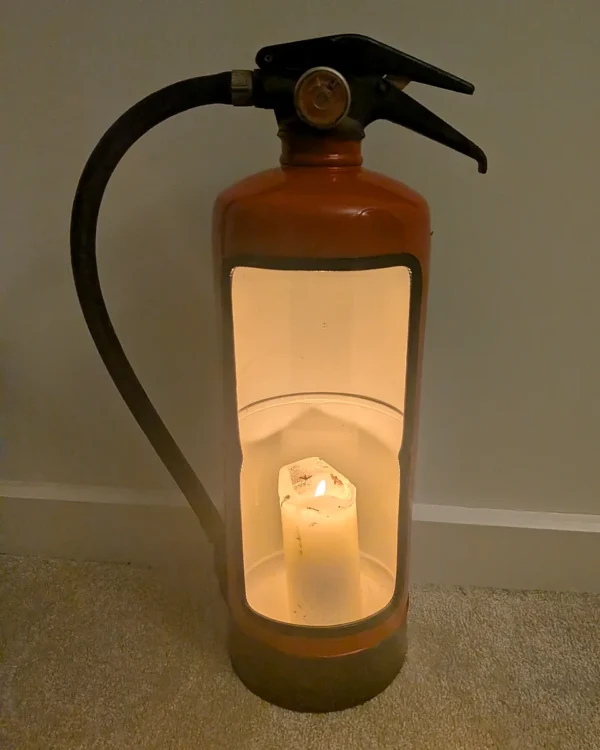 Red upcycled fire extinguisher candle holder with a glowing pillar candle and original black hose.