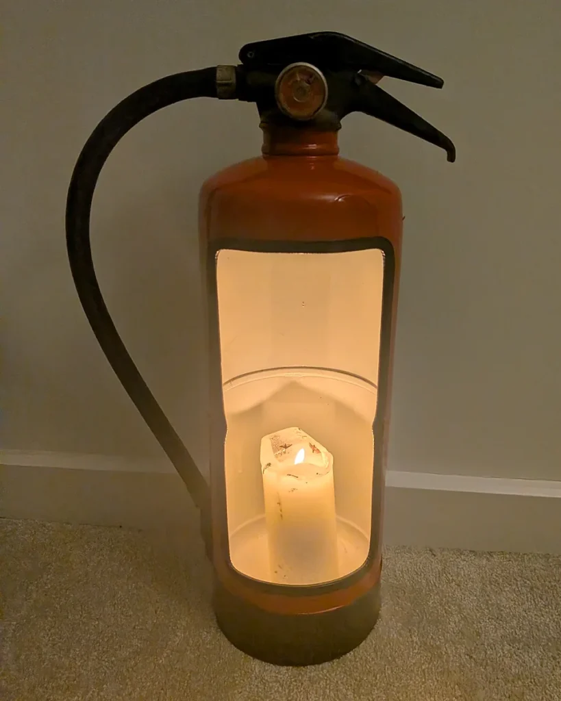 Red upcycled fire extinguisher candle holder with a glowing pillar candle and original black hose.