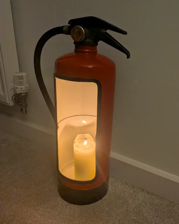 Angled front view of a red upcycled fire extinguisher candle holder with a black-trimmed opening.