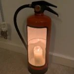 Upcycled fire extinguisher candle holder photographed in low light with a warm glow inside.
