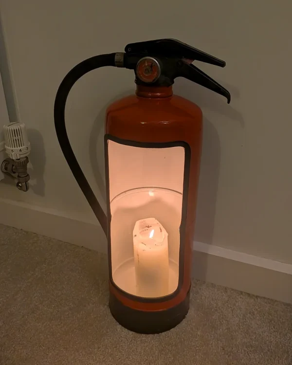 Upcycled fire extinguisher candle holder photographed in low light with a warm glow inside.