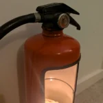 Close-up of the handle, pressure gauge and curved shoulder of the red fire extinguisher candle holder.