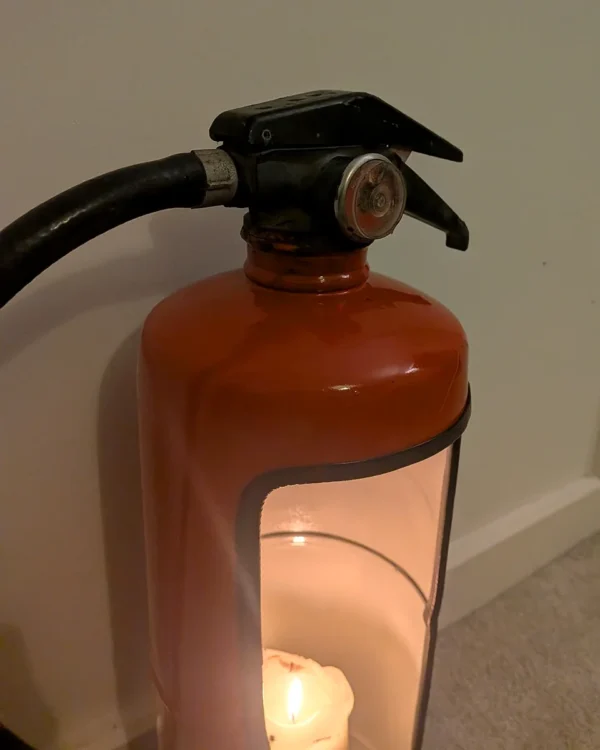 Close-up of the handle, pressure gauge and curved shoulder of the red fire extinguisher candle holder.