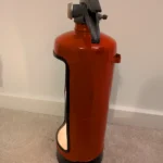 Side view of the red upcycled fire extinguisher candle holder showing the cut-out opening and black base.