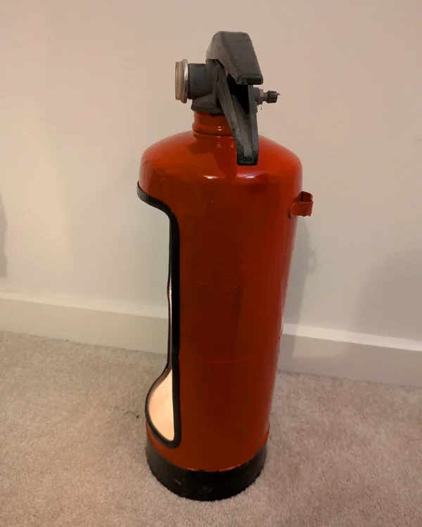 Side view of the red upcycled fire extinguisher candle holder showing the cut-out opening and black base.