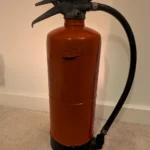 Rear view of the red upcycled fire extinguisher candle holder showing its original hose and handle.