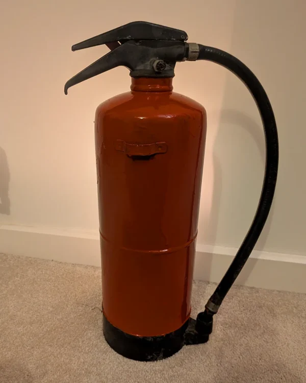Rear view of the red upcycled fire extinguisher candle holder showing its original hose and handle.