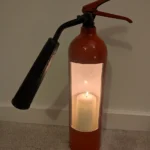 Front view of upcycled red CO2 fire extinguisher candle holder #8 with a lit pillar candle and original black horn.