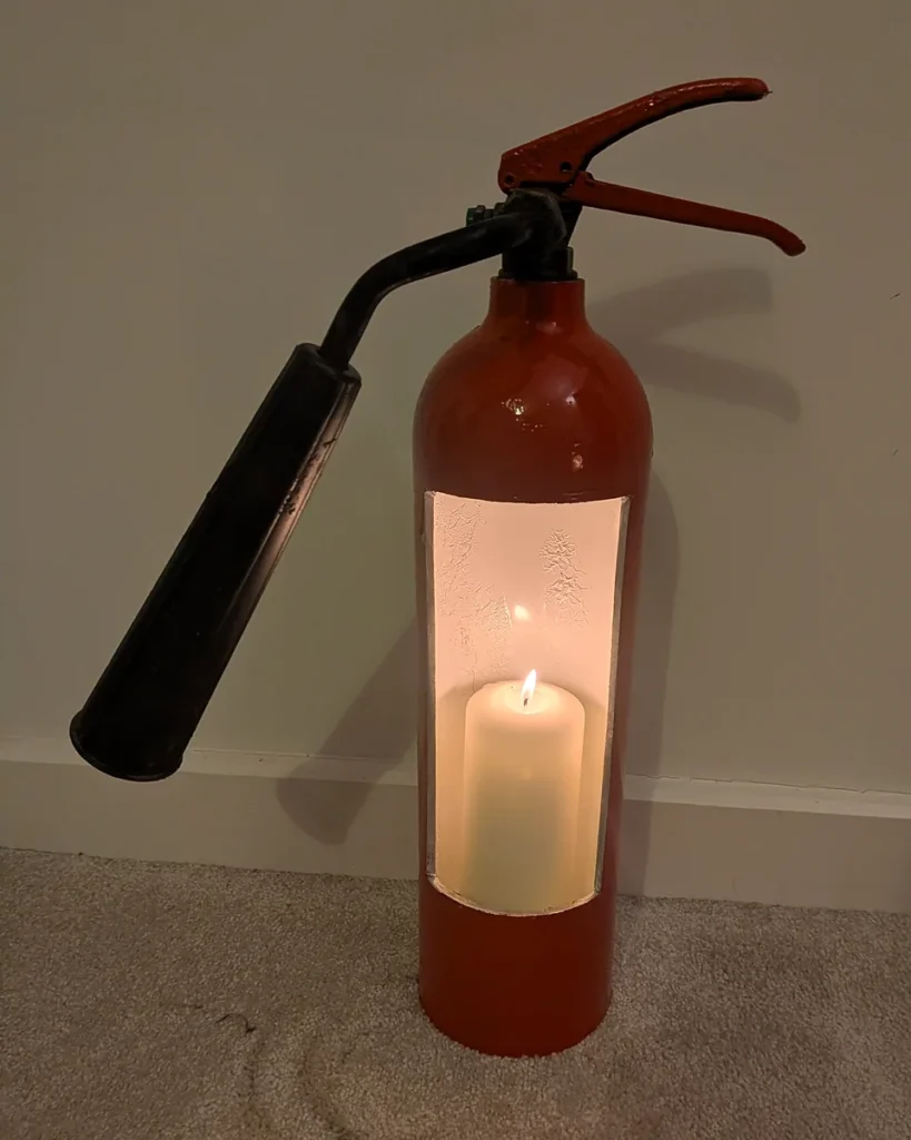 Front view of upcycled red CO2 fire extinguisher candle holder #8 with a lit pillar candle and original black horn.