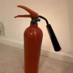 Rear view of upcycled red CO2 fire extinguisher candle holder #8 with its original handle and black discharge horn.