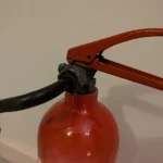 Close-up of the original handle, valve and red shoulder of upcycled fire extinguisher candle holder #8.