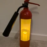 Full view of upcycled fire extinguisher candle holder #8 with a glowing LED candle and original black horn.