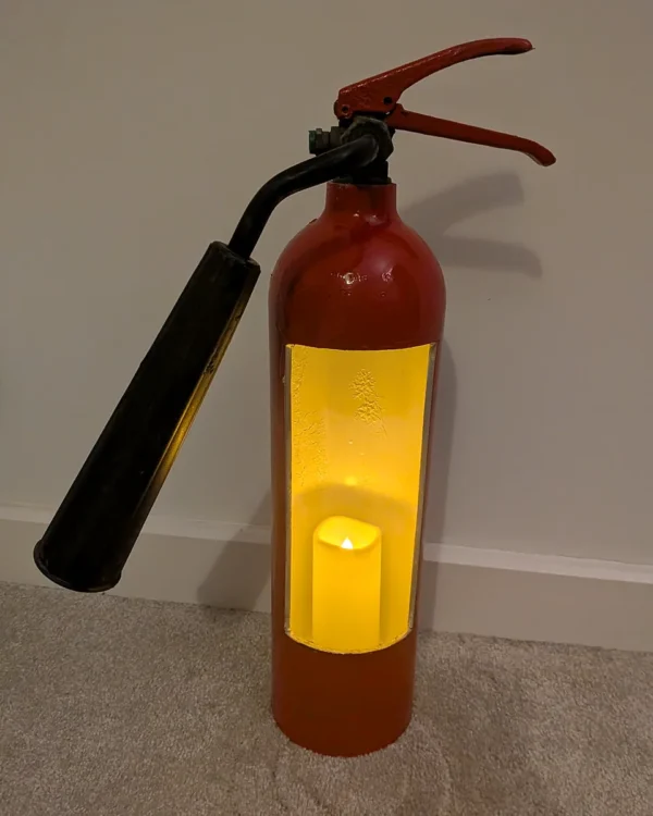 Full view of upcycled fire extinguisher candle holder #8 with a glowing LED candle and original black horn.