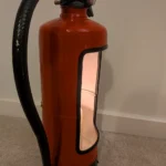 Side view of upcycled fire extinguisher candle holder #9 showing the original hose, red body and illuminated opening.