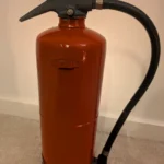 Rear view of red upcycled fire extinguisher candle holder #9 with its original black hose and handle.