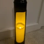 Full view of an upcycled nitrous oxide canister candle holder with a lit tealight at the base of the tall opening.