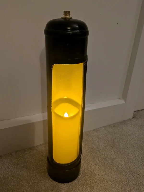 Full view of an upcycled nitrous oxide canister candle holder with a lit tealight at the base of the tall opening.