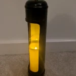 Upcycled black nitrous oxide canister candle holder with a glowing LED candle, white-painted interior and black opening trim.