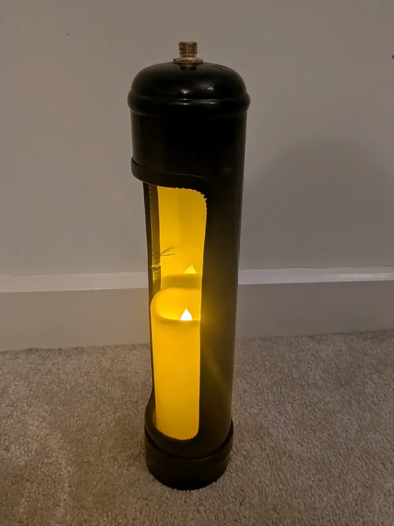 Upcycled black nitrous oxide canister candle holder with a glowing LED candle, white-painted interior and black opening trim.