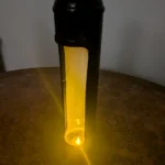 Upcycled nitrous canister candle holder displayed on a coin-covered table with a lit tealight inside.