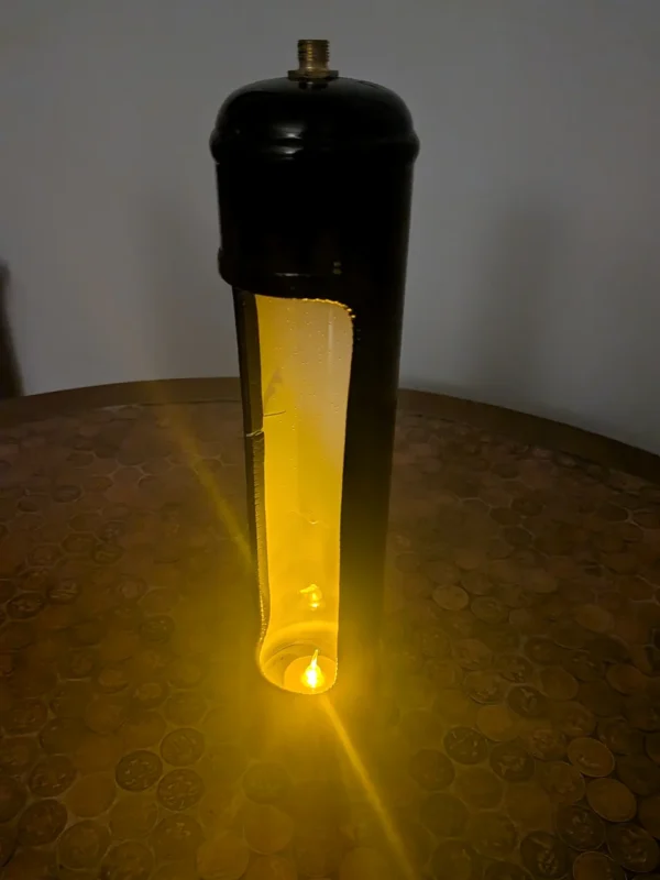 Upcycled nitrous canister candle holder displayed on a coin-covered table with a lit tealight inside.