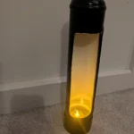 Angled view of a black upcycled nitrous canister candle holder showing the tall opening and warm LED candlelight.