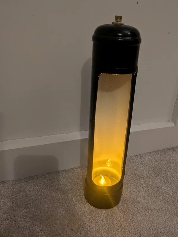 Angled view of a black upcycled nitrous canister candle holder showing the tall opening and warm LED candlelight.